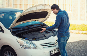 A puzzled man looking under the hood of his car trying to identify the problem.